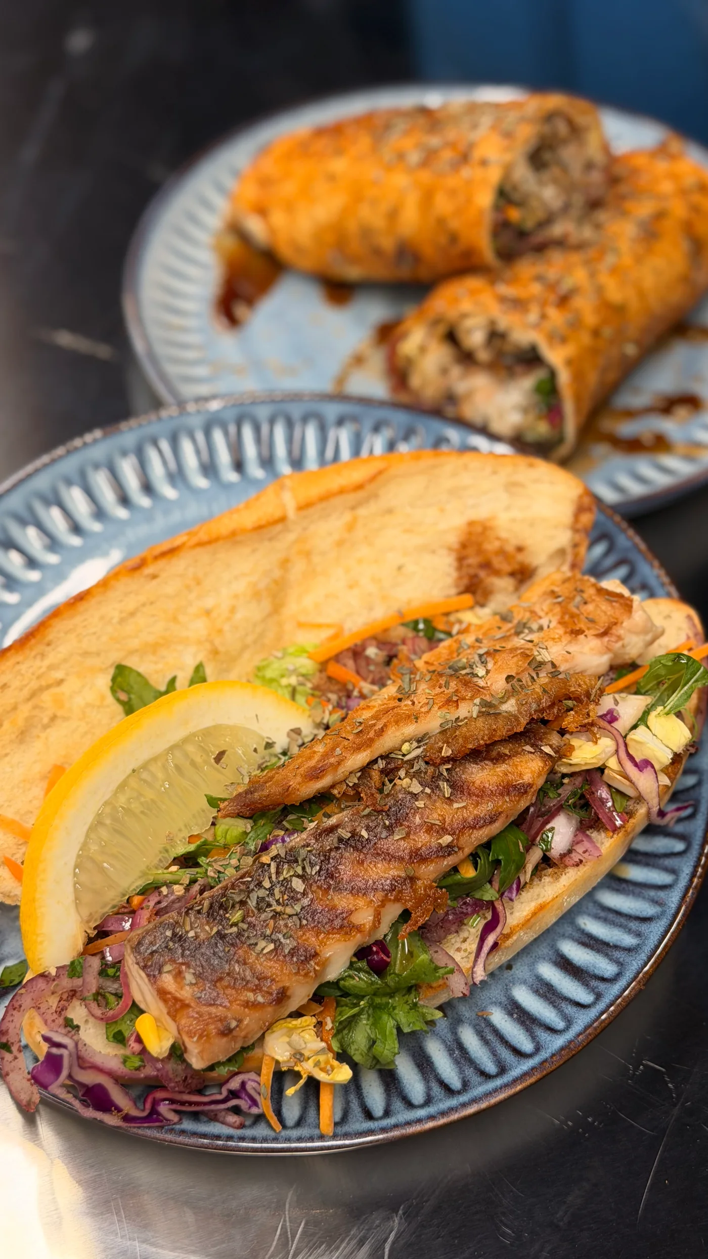 Grilled barramundi roll with fresh salad and lemon on a blue plate